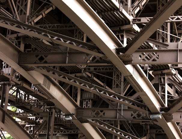 Intricate metal beams and structures form an elaborate framework, showcasing industrial design and engineering. The complex web of girders features rivets and cross-bracing against a backdrop of masonry.