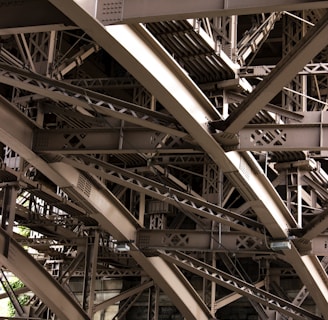 Intricate metal beams and structures form an elaborate framework, showcasing industrial design and engineering. The complex web of girders features rivets and cross-bracing against a backdrop of masonry.